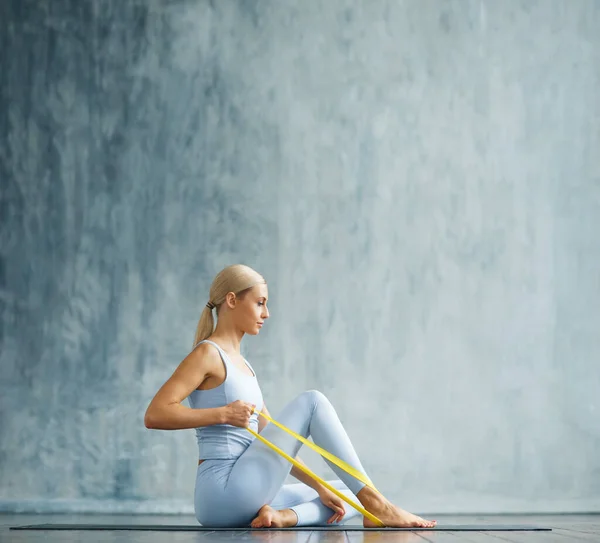 Ung smal blond kvinna i sportkläder är engagerad i fitness i ett rymligt träningsrum. Idrott, hälsa, gymnastik och livsstil. — Stockfoto