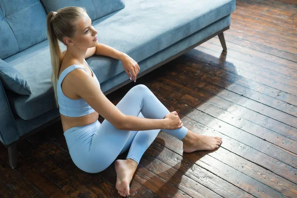 Jovem, em forma e esbelta mulher em sportswear está sentado no chão em casa e relaxante. Imagens De Bancos De Imagens Sem Royalties