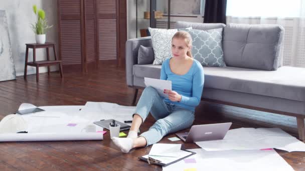 Молодая женщина работает с документами, используя ноутбук, сидя дома на полу. Студентка, предприниматель или девушка-фрилансер, работающая или обучающаяся дистанционно. Концепция дистанционного обучения и работы. — стоковое видео