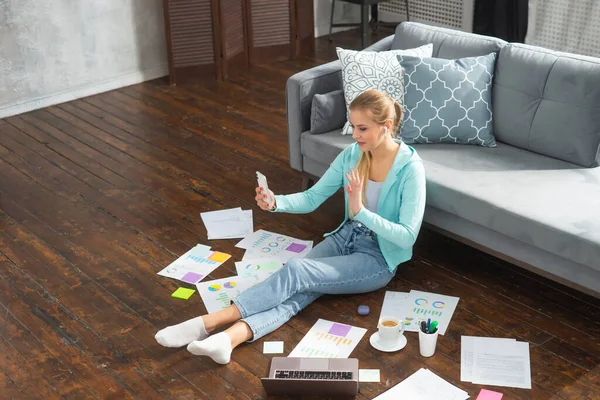 Mladá žena pracuje s dokumenty pomocí smartphonu a notebooku, zatímco sedí doma na podlaze. Student, podnikatel nebo na volné noze dívka pracující nebo studující na dálku přes internet. — Stock fotografie