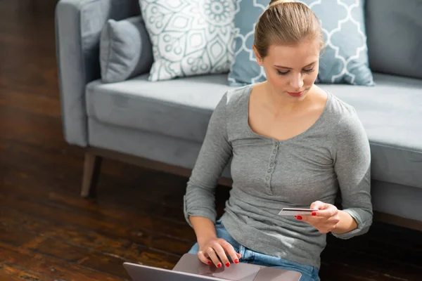 Une jeune femme commande des biens en ligne à l'aide d'un ordinateur portable et d'une carte de crédit. Achats, livraisons et systèmes de paiement en ligne concept. — Photo