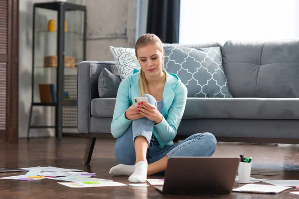 Mujer joven trabaja con documentos utilizando un ordenador portátil mientras está sentado en el suelo en casa. Estudiante, empresaria o freelancer que trabaja o estudia de forma remota a través de Internet. — Foto de Stock