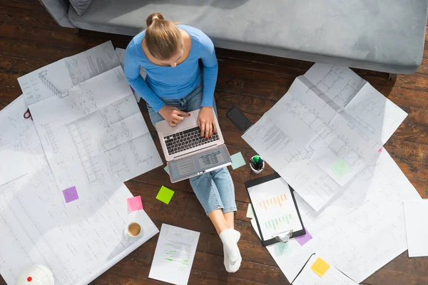 Giovane donna lavora con i documenti utilizzando un computer portatile mentre seduto sul pavimento a casa. Studente, imprenditrice o freelance che lavora o studia da remoto via internet. — Foto Stock