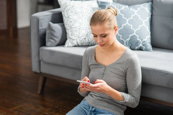 Junge Frau arbeitet mit Smartphone, während sie zu Hause auf dem Boden sitzt. Studentin, Unternehmerin oder Freiberuflerin, die aus der Ferne über das Internet arbeitet oder studiert. — Stockfoto