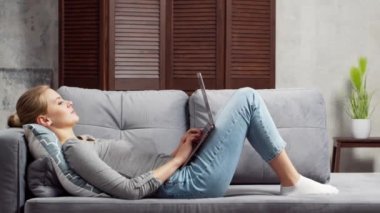 Genç bir kadın kanepede dizüstü bilgisayar kullanarak çalışıyor. Öğrenci, girişimci ya da serbest çalışan kız internet üzerinden çalışıyor ya da uzaktan öğrenim görüyor. Mesafe öğrenme ve iş kavramı.