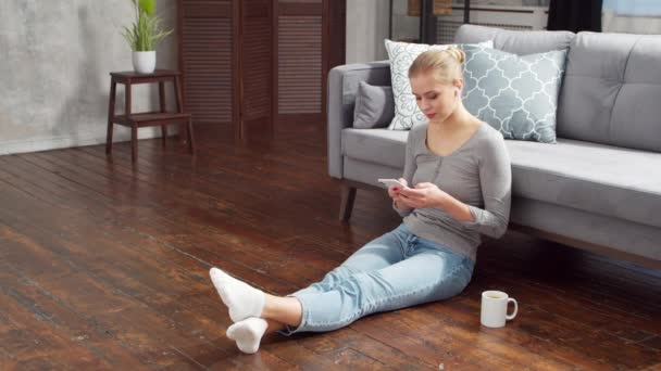 Mujer joven trabaja con el teléfono inteligente y el ordenador portátil mientras está sentado en el suelo en casa. Estudiante, empresaria o freelancer que trabaja o estudia a distancia. Concepto de aprendizaje a distancia y empleo. — Vídeos de Stock