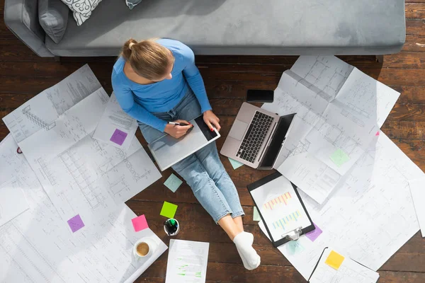 Giovane donna lavora con i documenti utilizzando un computer portatile mentre seduto sul pavimento a casa. Studente, imprenditrice o freelance che lavora o studia da remoto via internet. — Foto Stock