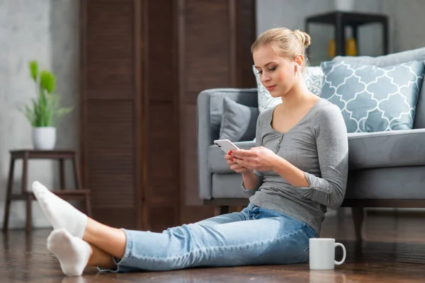 Mujer joven trabaja con un ordenador portátil y un teléfono inteligente mientras está sentado en el suelo en casa. Estudiante, empresaria o freelancer que trabaja o estudia de forma remota a través de Internet. —  Fotos de Stock