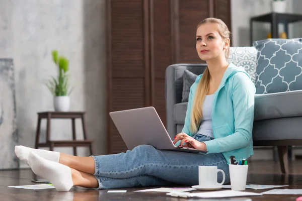 Mujer joven trabaja con documentos utilizando un ordenador portátil mientras está sentado en el suelo en casa. Estudiante, empresaria o freelancer que trabaja o estudia de forma remota a través de Internet. — Foto de Stock