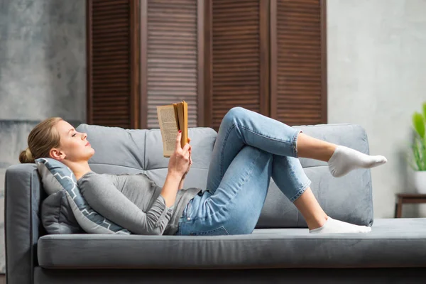 Junge blonde Mädchen lesen ein Buch oder ein Lehrbuch. Eine schöne Frau erholt sich zu Hause. — Stockfoto