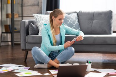 Genç bir kadın evde yerde otururken dizüstü bilgisayar kullanarak belgelerle çalışıyor. Öğrenci, girişimci veya serbest çalışan kız İnternet üzerinden çalışıyor veya uzaktan öğrenim görüyor.