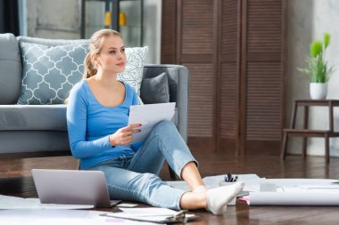 Genç bir kadın evde yerde otururken dizüstü bilgisayar kullanarak belgelerle çalışıyor. Öğrenci, girişimci veya serbest çalışan kız İnternet üzerinden çalışıyor veya uzaktan öğrenim görüyor.