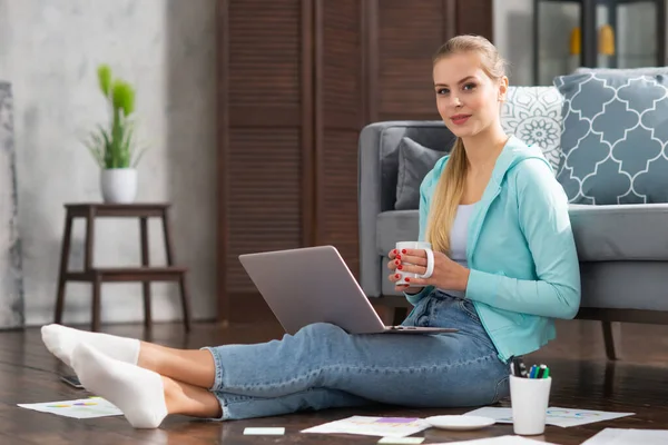 Ung kvinna arbetar med dokument med hjälp av en bärbar dator när du sitter på golvet hemma. Studerande, företagare eller frilansande flicka som arbetar eller studerar på distans via internet. — Stockfoto