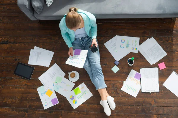 Ung kvinna arbetar med dokument när hon sitter på golvet hemma. Studerande, företagare eller frilansande flicka som arbetar eller studerar på distans via internet. — Stockfoto
