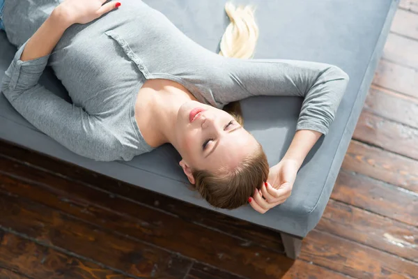 Joven chica hermosa se encuentra en un sofá. Mujer rubia feliz está descansando en casa. —  Fotos de Stock