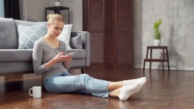 Genç kadın evde yerde otururken akıllı telefon ve dizüstü bilgisayar kullanıyor. Öğrenci, girişimci ya da serbest çalışan ya da uzaktan eğitim gören bir kız. Mesafe öğrenme ve iş kavramı.