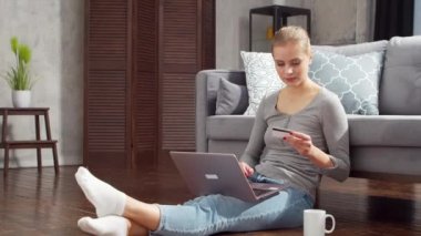Genç bir kadın internetten dizüstü bilgisayar ve kredi kartıyla mal sipariş ediyor. Çevrimiçi alışveriş, dağıtım ve ödeme sistemleri kavramı.