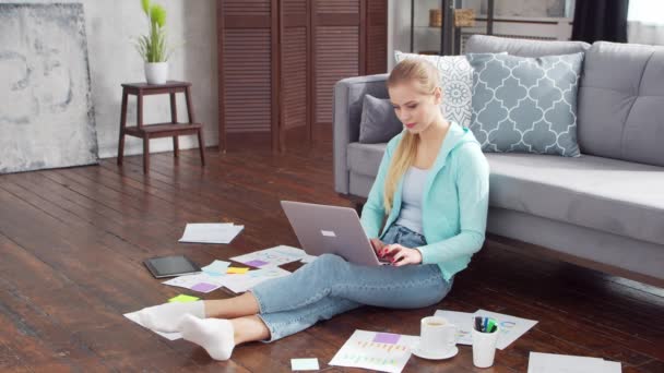 Wanita muda bekerja dengan dokumen menggunakan laptop saat duduk di lantai di rumah. Siswa, pengusaha atau gadis pekerja lepas bekerja atau belajar dari jarak jauh. Konsep pembelajaran jarak jauh dan pekerjaan. — Stok Video