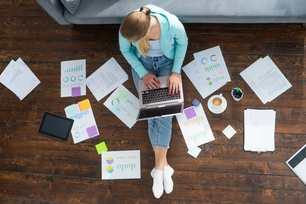 La jeune femme travaille avec des documents à l'aide d'un ordinateur portable alors qu'elle est assise sur le sol à la maison. Étudiant, entrepreneur ou freelance fille travaillant ou étudiant à distance via Internet. — Photo