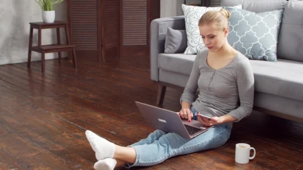 Mujer joven trabaja con documentos utilizando un ordenador portátil mientras está sentado en el suelo en casa. Estudiante, empresaria o freelancer que trabaja o estudia a distancia. Enseñanza a distancia y concepto de trabajo. — Vídeo de stock