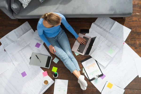 Junge Frau arbeitet mit Laptop mit Dokumenten, während sie zu Hause auf dem Boden sitzt. Studentin, Unternehmerin oder Freiberuflerin, die aus der Ferne über das Internet arbeitet oder studiert. — Stockfoto