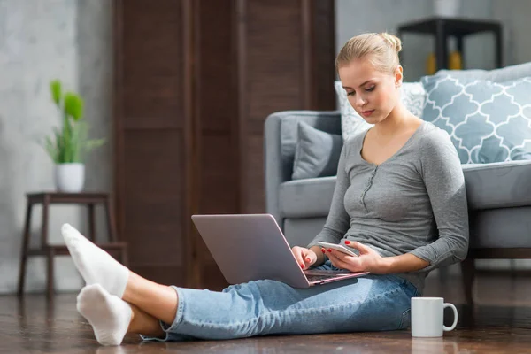 Mujer joven trabaja usando un ordenador portátil mientras está sentado en el suelo en casa. Estudiante, empresaria o freelancer que trabaja o estudia de forma remota a través de Internet. — Foto de Stock