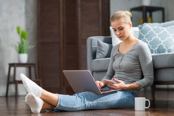 Young woman works using a laptop while sitting on the floor at home. Student, entrepreneur or freelancer girl working or studying remotely via internet.