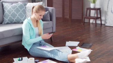 Genç bir kadın evde yerde otururken dizüstü bilgisayar kullanarak belgelerle çalışıyor. Öğrenci, girişimci ya da serbest çalışan ya da uzaktan eğitim gören bir kız. Mesafe öğrenme ve iş kavramı.