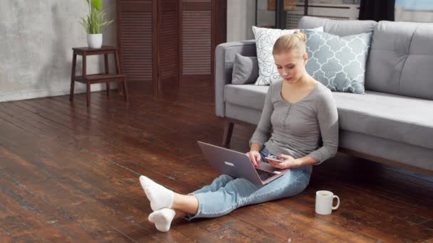 La jeune femme travaille avec des documents à l'aide d'un ordinateur portable alors qu'elle est assise sur le sol à la maison. Étudiante, entrepreneure ou pigiste travaillant ou étudiant à distance. Enseignement à distance et concept d'emploi. — Video