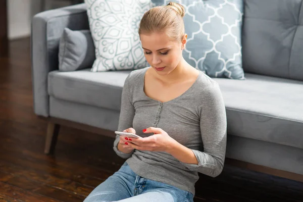 Mujer joven trabaja usando un teléfono inteligente mientras está sentada en el suelo en casa. Estudiante, empresaria o freelancer que trabaja o estudia de forma remota a través de Internet. —  Fotos de Stock