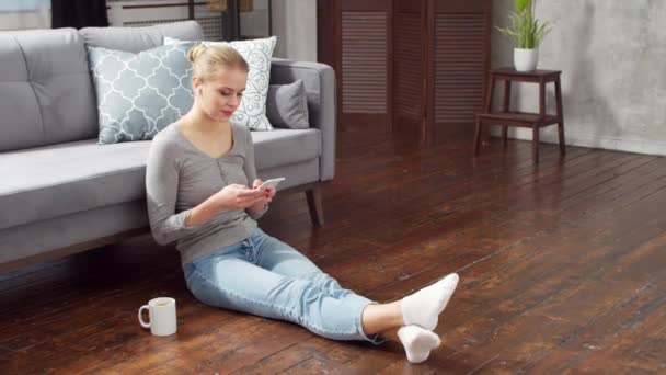 Jeune femme travaille en utilisant un smartphone et un ordinateur portable tout en étant assis sur le sol à la maison. Étudiante, entrepreneure ou pigiste travaillant ou étudiant à distance. Le concept d'enseignement à distance et d'emploi. — Video