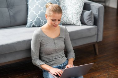 Genç bir kadın evde yerde otururken dizüstü bilgisayar kullanıyor. Öğrenci, girişimci veya serbest çalışan kız İnternet üzerinden çalışıyor veya uzaktan öğrenim görüyor.