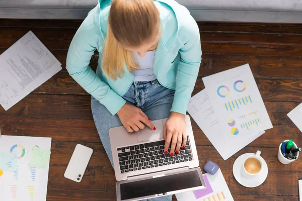 Junge Frau arbeitet mit Laptop mit Dokumenten, während sie zu Hause auf dem Boden sitzt. Studentin, Unternehmerin oder Freiberuflerin, die aus der Ferne über das Internet arbeitet oder studiert. — Stockfoto