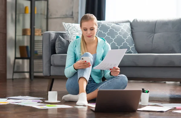 Mujer joven trabaja con documentos utilizando un ordenador portátil mientras está sentado en el suelo en casa. Estudiante, empresaria o freelancer que trabaja o estudia de forma remota a través de Internet. —  Fotos de Stock