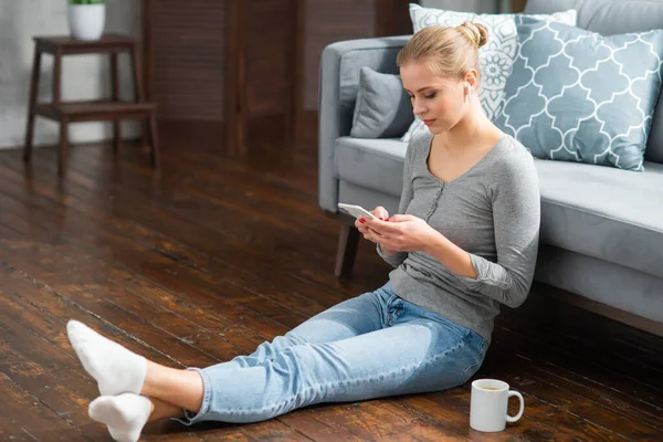 Jovem trabalha usando um laptop e smartphone enquanto está sentado no chão em casa. Estudante, empreendedora ou freelancer trabalhando ou estudando remotamente via internet. — Fotografia de Stock