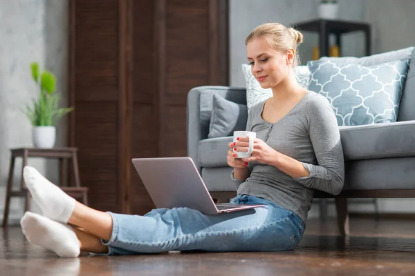 Mujer joven trabaja usando un ordenador portátil mientras está sentado en el suelo en casa. Estudiante, empresaria o freelancer que trabaja o estudia de forma remota a través de Internet. — Foto de Stock