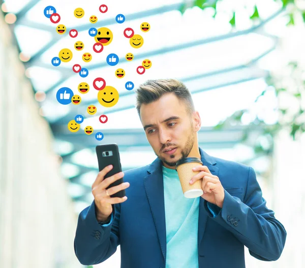 Giovane influencer di successo o blogger guarda un feed di notizie di social network, ottiene Mi piace e visualizzazioni sotto forma di emoji animati. Il concetto di social media, internet e comunicazione online. — Foto Stock