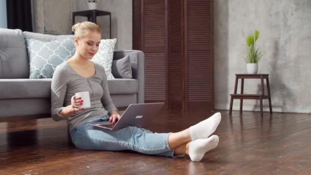 La jeune femme travaille avec des documents à l'aide d'un ordinateur portable alors qu'elle est assise sur le sol à la maison. Étudiante, entrepreneure ou pigiste travaillant ou étudiant à distance. Enseignement à distance et concept d'emploi. — Video