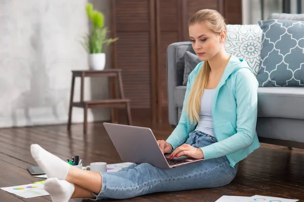 젊은 여자는 집 바닥에 앉아 있는 동안 노트북을 사용하는 서류를 가지고 일한다. 학생, 사업가 또는 프리랜서 소녀는 인터넷을 통해 원격으로 일하거나 공부 합니다.. — 스톡 사진