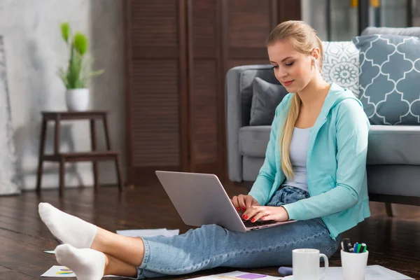 Mujer joven trabaja con documentos utilizando un ordenador portátil mientras está sentado en el suelo en casa. Estudiante, empresaria o freelancer que trabaja o estudia de forma remota a través de Internet. —  Fotos de Stock