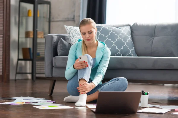 Giovane donna lavora con i documenti utilizzando un computer portatile mentre seduto sul pavimento a casa. Studente, imprenditrice o freelance che lavora o studia da remoto via internet. — Foto Stock