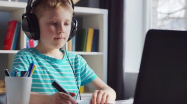 Çocuk Masa 'da ödevini yapıyor. Şirin Çocuk Laptop Bilgisayar ve Okul Ders Kitapları 'nın yardımıyla Evde Öğreniyor. Eğitim ve Uzaktan Eğitim Konsepti.