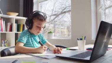 Çocuk Masa 'da ödevini yapıyor. Şirin Çocuk Laptop Bilgisayar ve Okul Ders Kitapları 'nın yardımıyla Evde Öğreniyor. Eğitim ve Uzaktan Eğitim Konsepti.