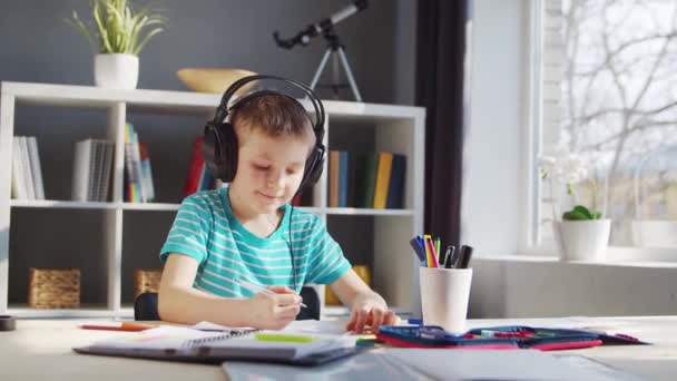 De jongen doet zijn huiswerk aan de tafel. Schattig kind is thuis leren met behulp van lesboeken en schoolmaterialen. Studie en onderwijs Concept. — Stockvideo