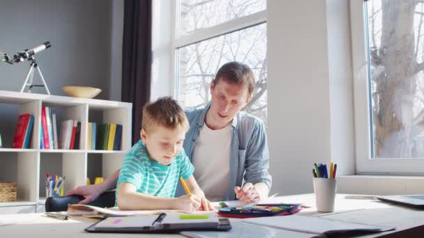 Junge und Vater erledigen Hausaufgaben am Tisch. Nettes Kind lernt zu Hause mit Hilfe von Lehrbüchern und Schulmaterialien. Das Konzept von Studium und Ausbildung. — Stockvideo