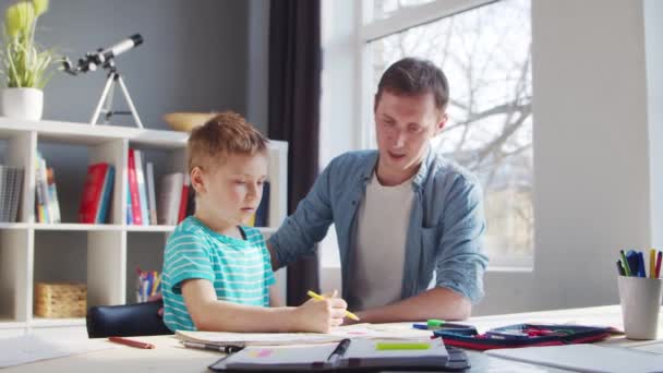 O rapaz e o pai estão a fazer os trabalhos de casa na mesa. Criança Bonita está aprendendo em casa com a ajuda de livros didáticos e materiais escolares. O Conceito de Estudo e Educação. — Vídeo de Stock