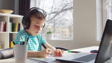 Çocuk Masa 'da ödevini yapıyor. Şirin Çocuk Laptop Bilgisayar ve Okul Ders Kitapları 'nın yardımıyla Evde Öğreniyor. Eğitim ve Uzaktan Eğitim Konsepti.