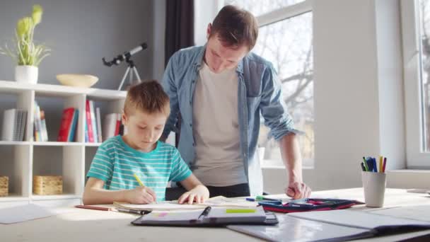 Jongen en vader doen huiswerk aan tafel. Schattig kind is thuis leren met behulp van lesboeken en schoolmaterialen. Het concept van studie en onderwijs. — Stockvideo