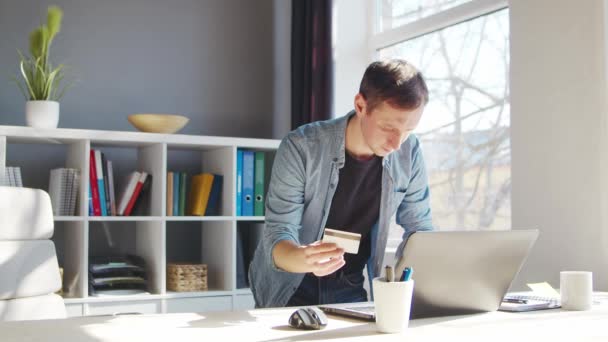 Le jeune homme fait des achats sur Internet à l'aide d'une carte de crédit bancaire. La personne travaille à la maison à l'ordinateur. Concept de systèmes d'achat et de paiement en ligne. — Video