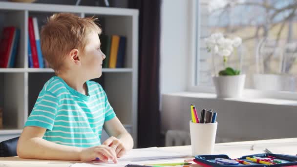 Chłopak odrabia lekcje przy stole. Słodkie dziecko uczy się w domu z pomocą podręczników i materiałów szkolnych. Koncepcja studiów i edukacji. — Wideo stockowe